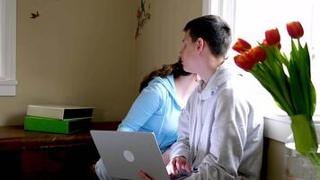 a boy and a girl and teenagers solve homework on a computer laptops they turn around at the same time and look out window wondering what to watch together to be distracted from studying adolescence video