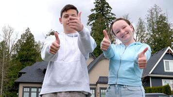 jongen en meisje tieners hebben pret tonen duimen omhoog vreugde geluk Aan de straat in een privaat kwartaal plaats voor tekst in beweging luxe huizen privaat sector relaties vreugde adolescentie video