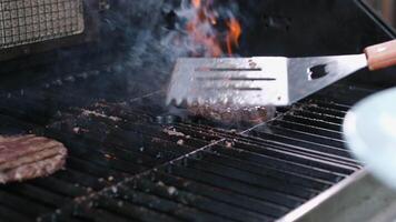 Two burger patties char and smoke on grill grates over open flame in commercial restaurant kitchen, slow motion 4k video