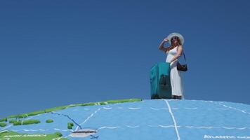 young girl in white dress and huge hat with a suitcase travels around globe Close up woman legs walks on asphalt road and traveling world with travel suitcase . Female hitchhiking around country video