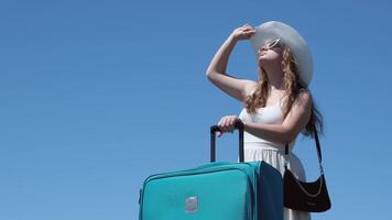 young girl in white dress and huge hat with a suitcase travels around globe Close up woman legs walks on asphalt road and traveling world with travel suitcase . Female hitchhiking around country video