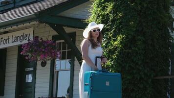 CN Fort Langley Girl waiting for train station stands at the train station waiting for the train travel trip white clothes dress hat. Huge green suitcase video