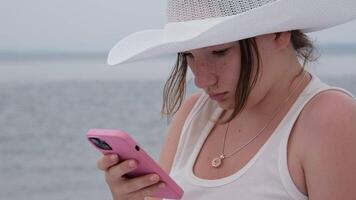 meisje gebruik makend van mobiele telefoon Aan een zee oceaan oever. jong meisje Aan de strand met uw smartphone. video