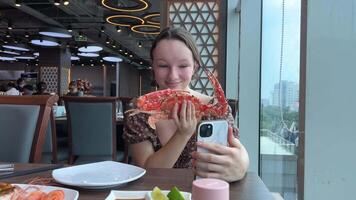 een meisje eet een groot sneeuw krab in een restaurant, onderzoekt de reusachtig klauwen, duurt foto's, en schrijft een blog over de correct snijdend van zeevruchten. video