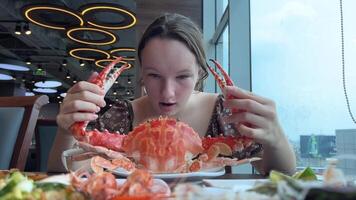 A girl eats a large snow crab in a restaurant, examines the huge claws, takes photographs, and writes a blog about the correct cutting of seafood. video