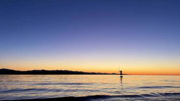 sunset on Pacific Ocean calm silhouette of man floating paddle he is literally a point against the background of nature, you can see the red and orange line of the horizon the sea and the sky evening video