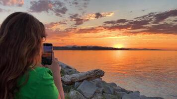 ragazza testi e pergamene utilizzando Telefono sociale media applicazioni a tramonto cielo mare ventoso sfondo avvicinamento lento movimento. tecnologie sviluppo Pericolo di schermo dipendenza vs godendo natura concetto video