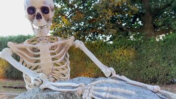 The skeleton stands near the tombstone and holds on to it looks down it is in the cemetery Halloween holiday in autumn it is possible to use it as a background for some text the camera slowly floats video