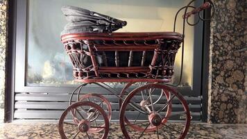 Wicker pram against the background of a fireplace Toy work of art thin wheels like from a cart Slightly intimidating Brown wood and bMarble tiles around the fireplacelack fabric inside video