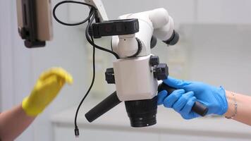 close-up of microscope in dental clinic hands of nurse and doctor set up equipment tablet and microscope to work with patient filling canals with latest technology unrecognizable people video