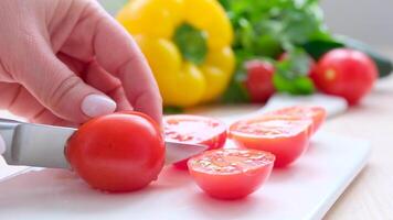 femmina mani tagliare ciliegia pomodori su bianca taglio tavola coltello tagli pomodoro nel metà delizioso pomodoro succo flussi su nel verdure giallo campana Pepe coriandolo cetrioli cucinando insalata affettare verdure video