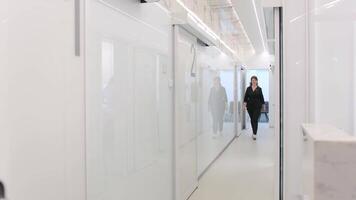 A woman in black walks along a long white corridor, a doctor in black clothes video