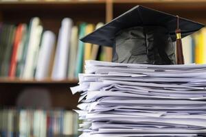 un graduación soltero gorra en un apilar de papel, nuevo graduado trabajo caza concepto. foto