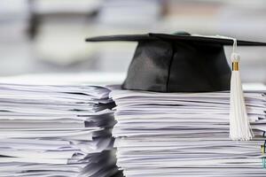 un graduación soltero gorra en un apilar de papel, nuevo graduado trabajo caza concepto. foto