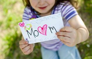 Little girl giving her hand writing greeting card to her mom. photo