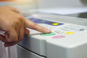 The office secretary presses the button to start the document copying machine to have another copy of the document stored in a file as evidence. . photo