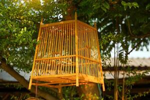 A wooden birdcage hangs on a tree in front of a community shop selling wooden products. Soft and selective focus. photo