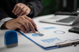 Businessman Analyzing Pie Chart and Graph Data with Pen on Desk With Laptop and Smartphone photo