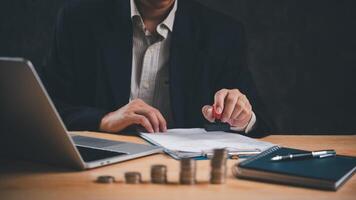 Man in a suit stamp approves documents at a wooden desk with a laptop and coins. business finance and banking concept. photo