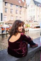 a girl in a red corduroy dress with an open back walks through the streets of Bruges on an autumn day photo