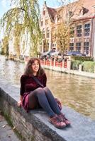 a girl in a red corduroy dress with an open back walks through the streets of Bruges on an autumn day photo