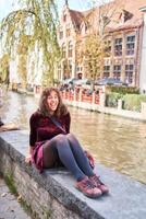 a girl in a red corduroy dress with an open back walks through the streets of Bruges on an autumn day photo