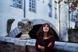 a girl in a red corduroy dress with an open back walks through the streets of Bruges on an autumn day photo