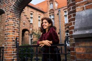 a girl in a red corduroy dress with an open back walks through the streets of Bruges on an autumn day photo