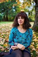 un niña en un vestir con globos mentiras en el suelo cubierto con otoño hojas foto