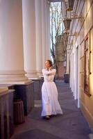 elegante medio años mujer en blanco Clásico vestir cerca teatro con antiguo columnatas foto