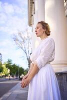 elegant middle age woman in white vintage dress near theater with antique colonnades photo