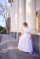 elegante medio años mujer en blanco Clásico vestir cerca teatro con antiguo columnatas foto