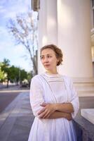 elegante medio años mujer en blanco Clásico vestir cerca teatro con antiguo columnatas foto