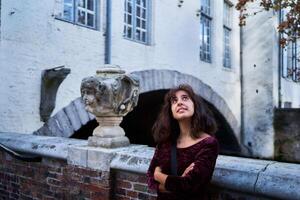 a girl in a red corduroy dress with an open back walks through the streets of Bruges on an autumn day photo