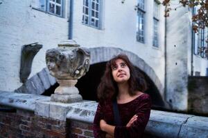 a girl in a red corduroy dress with an open back walks through the streets of Bruges on an autumn day photo