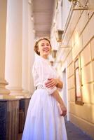 elegante medio años mujer en blanco Clásico vestir cerca teatro con antiguo columnatas foto