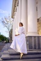 elegant middle age woman in white vintage dress near theater with antique colonnades photo