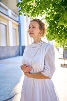 elegante medio años mujer en un blanco Clásico vestir en contra el antecedentes de histórico edificios en el Mañana ligero foto