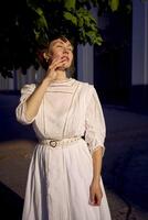 elegante medio años mujer en un blanco Clásico vestir en contra el antecedentes de histórico edificios en el Mañana ligero foto