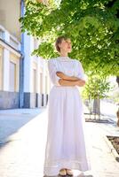 elegante medio años mujer en un blanco Clásico vestir en contra el antecedentes de histórico edificios en el Mañana ligero foto