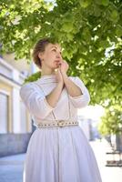 elegante medio años mujer en un blanco Clásico vestir en contra el antecedentes de histórico edificios en el Mañana ligero foto