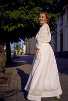 elegante medio años mujer en un blanco Clásico vestir en contra el antecedentes de histórico edificios en el Mañana ligero foto