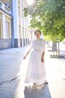 elegante medio años mujer en un blanco Clásico vestir en contra el antecedentes de histórico edificios en el Mañana ligero foto