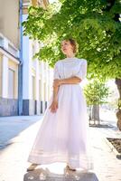 elegante medio años mujer en un blanco Clásico vestir en contra el antecedentes de histórico edificios en el Mañana ligero foto