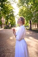 chic middle age woman in a white vintage dress in a sunlit alley photo