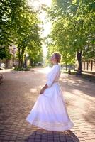 chic middle age woman in a white vintage dress in a sunlit alley photo