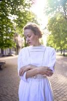 chic middle age woman in a white vintage dress in a sunlit alley photo