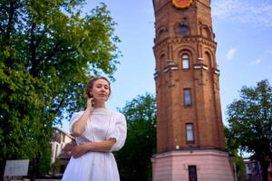 elegante joven mujer en un blanco Clásico vestir en el cuadrado cerca el histórico agua torre en vinnytsia foto