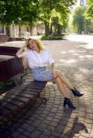 beautiful middle age woman in 70s, 80s style clothes on a bench in a sunlit avenue photo