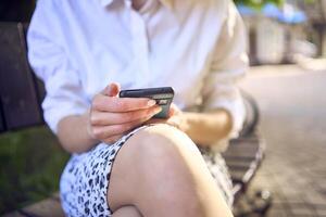 a beautiful middle age woman in 70s, 80s style clothes is looking at her smartphone on a bench photo